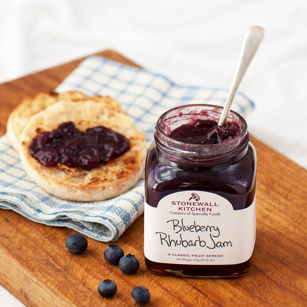 A kitchen counter with a Stonewall Kitchen's Blueberry Rhubarb Jam jar open with a biscuit and jam