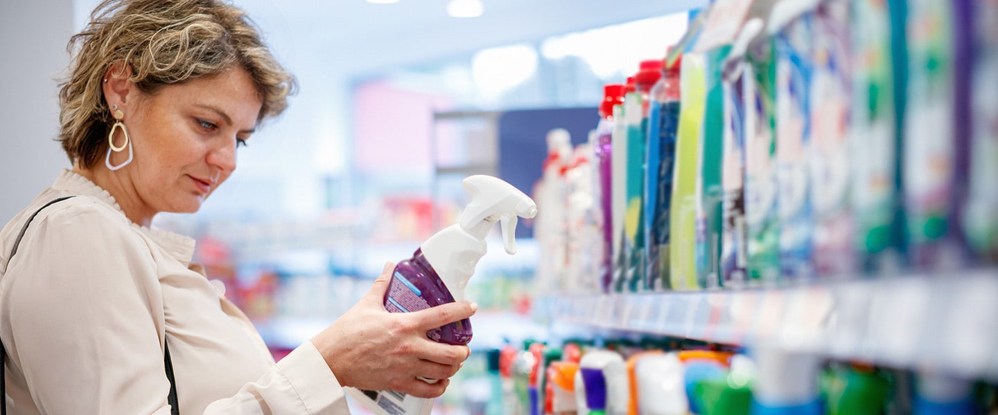 A woman inspects a spray bottle shrink sleeve in a store aisle